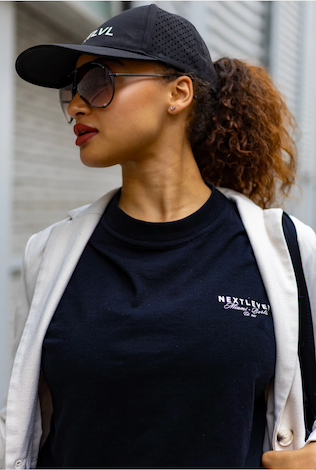 Woman wearing a black cap, sunglasses, and a navy blue turtleneck with 'Next Level' branding.